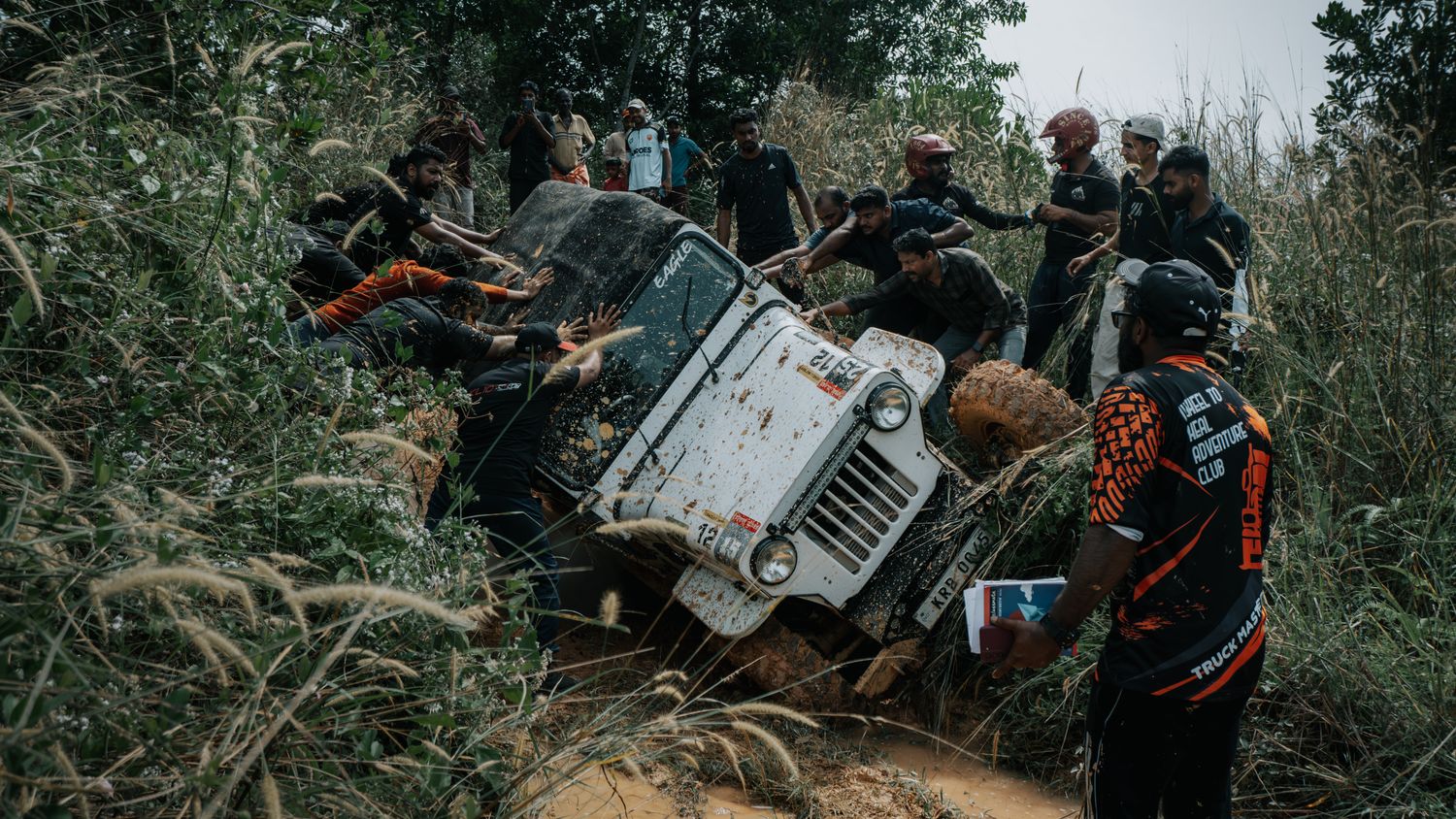 Group recovering a stuck off-road vehicle on a muddy trail where additional traction boards would shorten the extraction