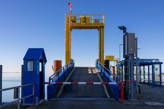 Vibrant yellow and blue ferry dock structure under clear skies in Dagebüll, Germany.