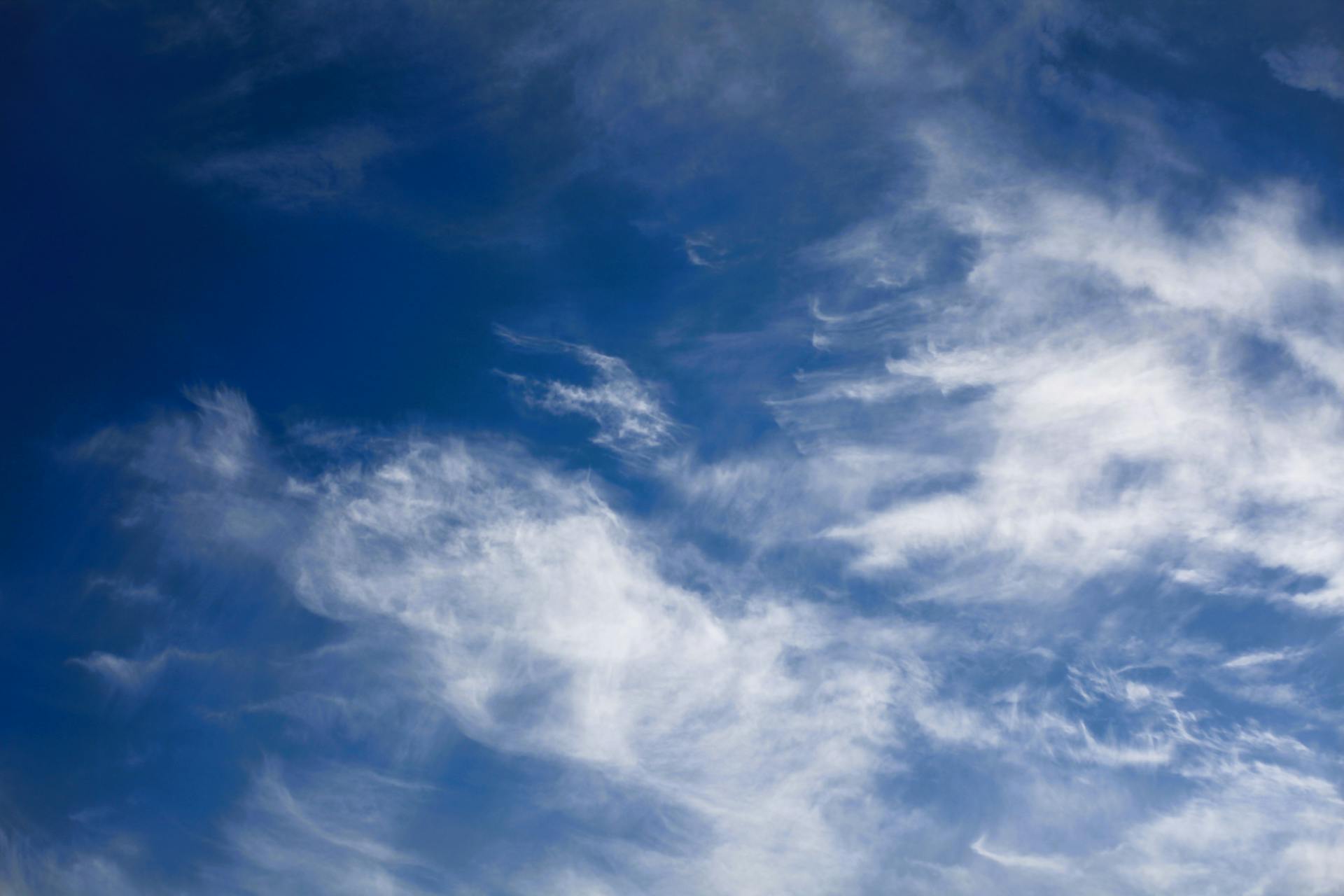 Bright blue sky with fluffy, wispy cirrus clouds in a peaceful setting.