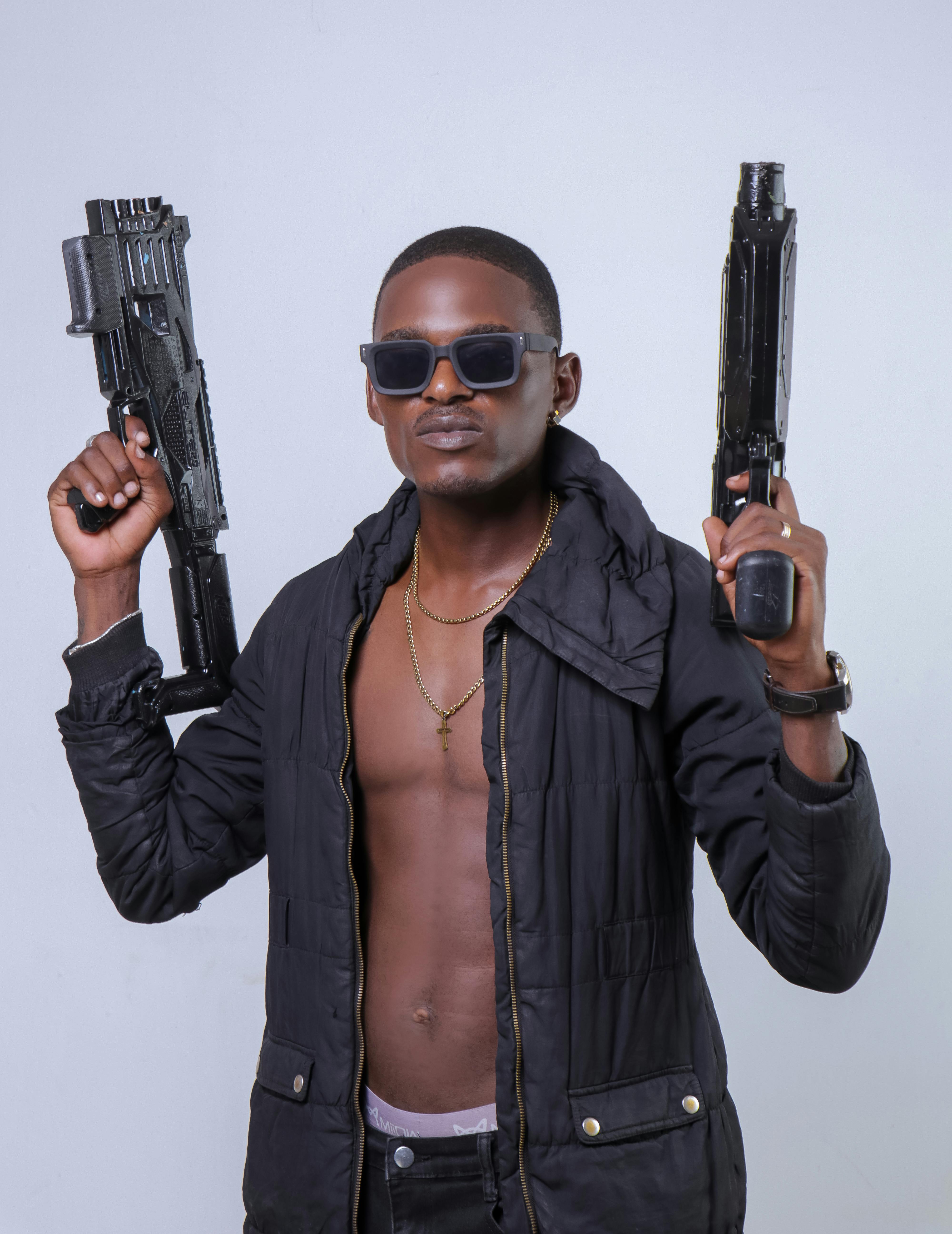 Portrait of a man holding toy guns, exuding confidence with a stylish look in a studio.