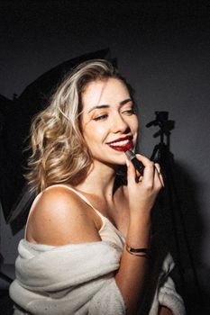 Elegant woman applying lipstick in a studio setting, showcasing beauty and confidence.