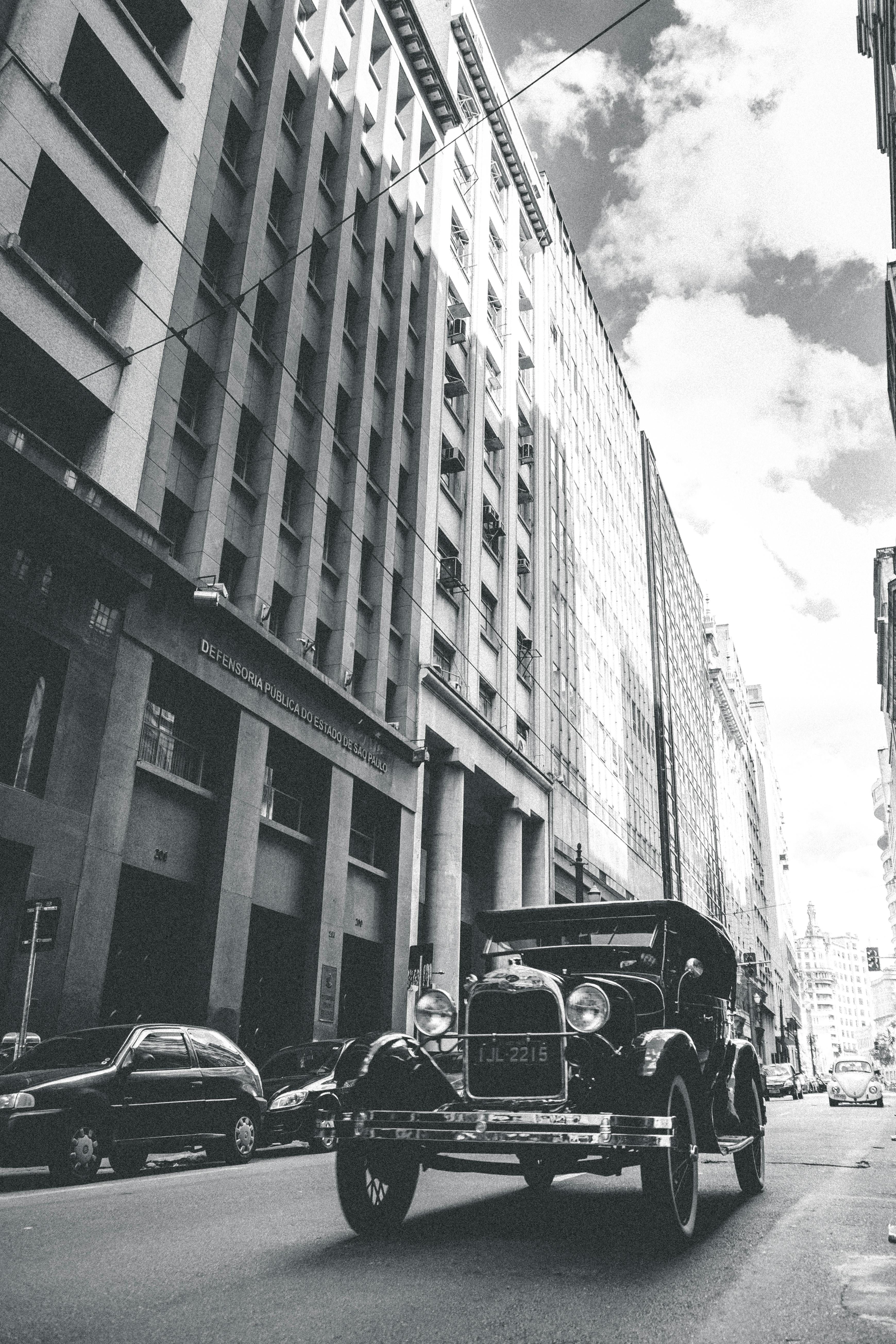 一辆老爷车驶过高楼林立的城市街道，天空多云