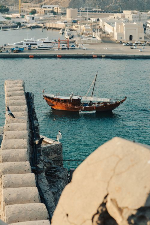 Free A traditional wooden dhow sailing vessel docked in Muscat, Oman’s harbor near historic fort wall. Stock Photo
