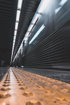 Contemporary interior of underground station with fast train departing from platform and yellow restrictive line
