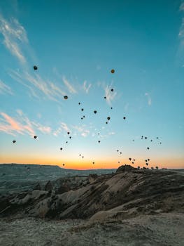 Stunning view of hot air balloons floating over Cappadocia's unique landscape during sunrise.