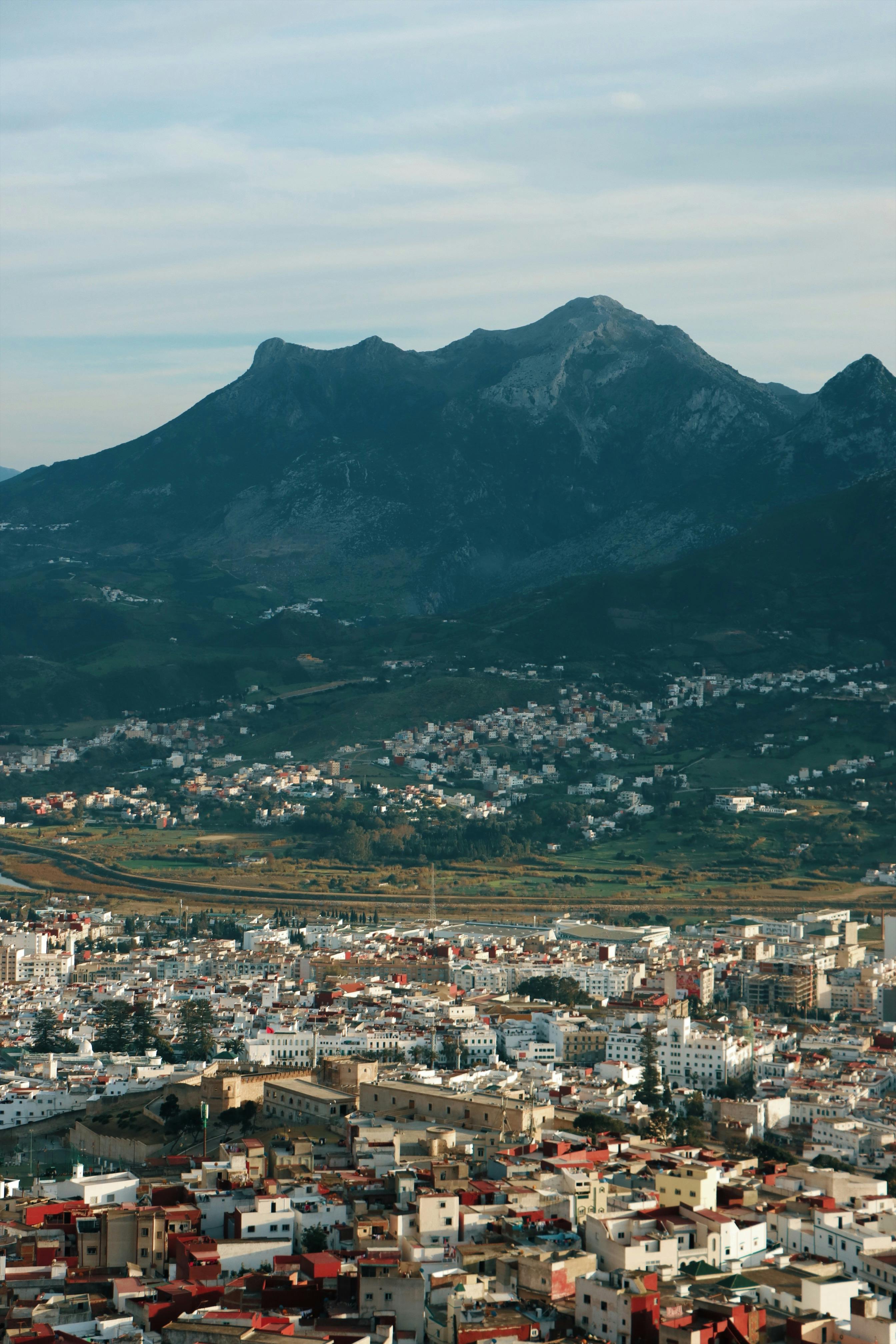 Aerial view of a city with a mountain backdrop under a cloudy sky.