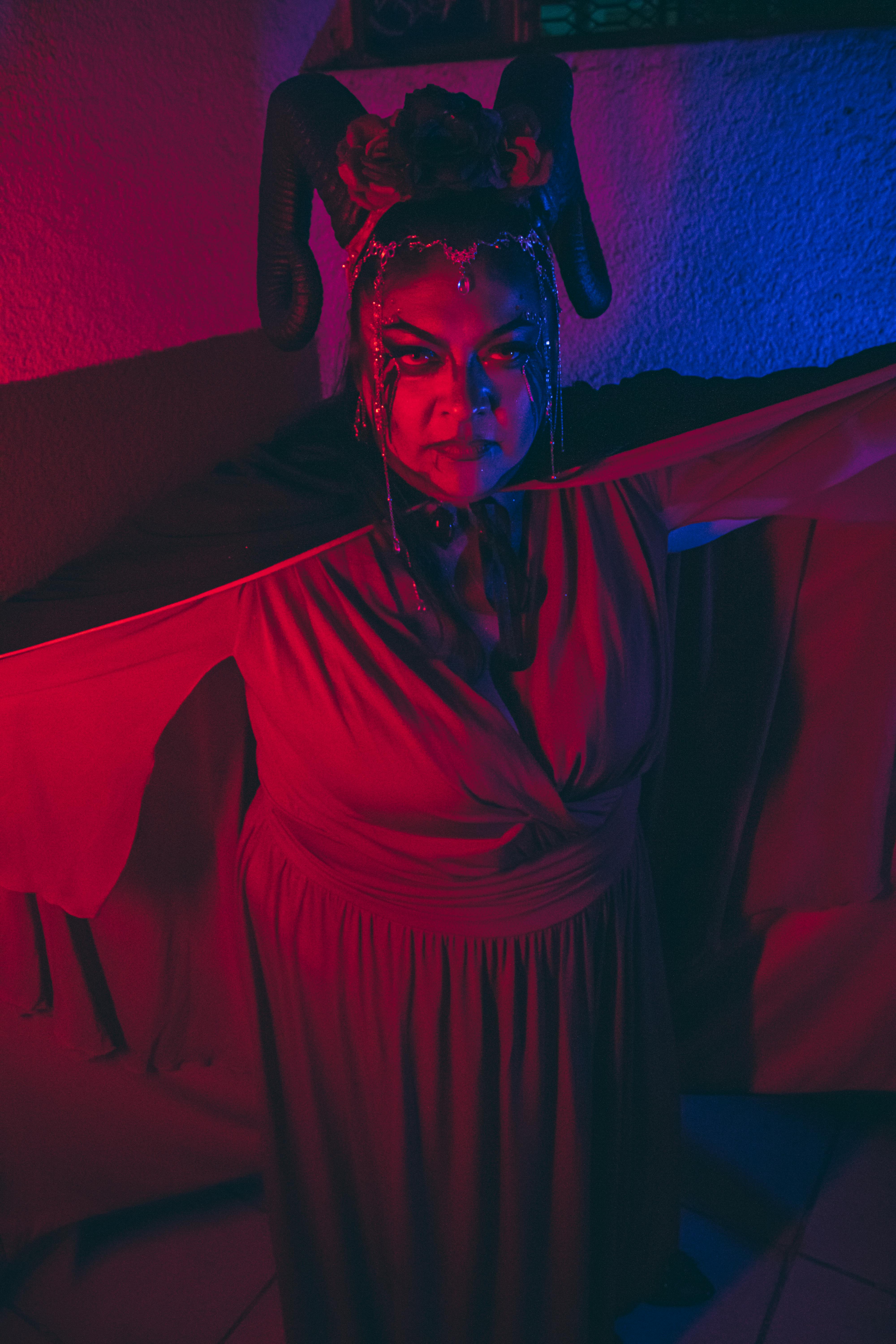 Ücretsiz Dramatik ışıklandırma altında boynuzlu makyaj ve kırmızı pelerin içeren canlı sanatsal portre. Stok Fotoğraflar