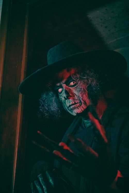 Free A frightening character with artistic makeup stands in a dimly lit room, creating an eerie atmosphere. Stock Photo