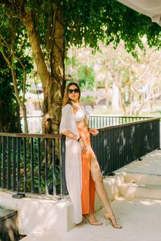 Elegant model in a stylish outfit posing outdoors under a tree in Bali, Indonesia.