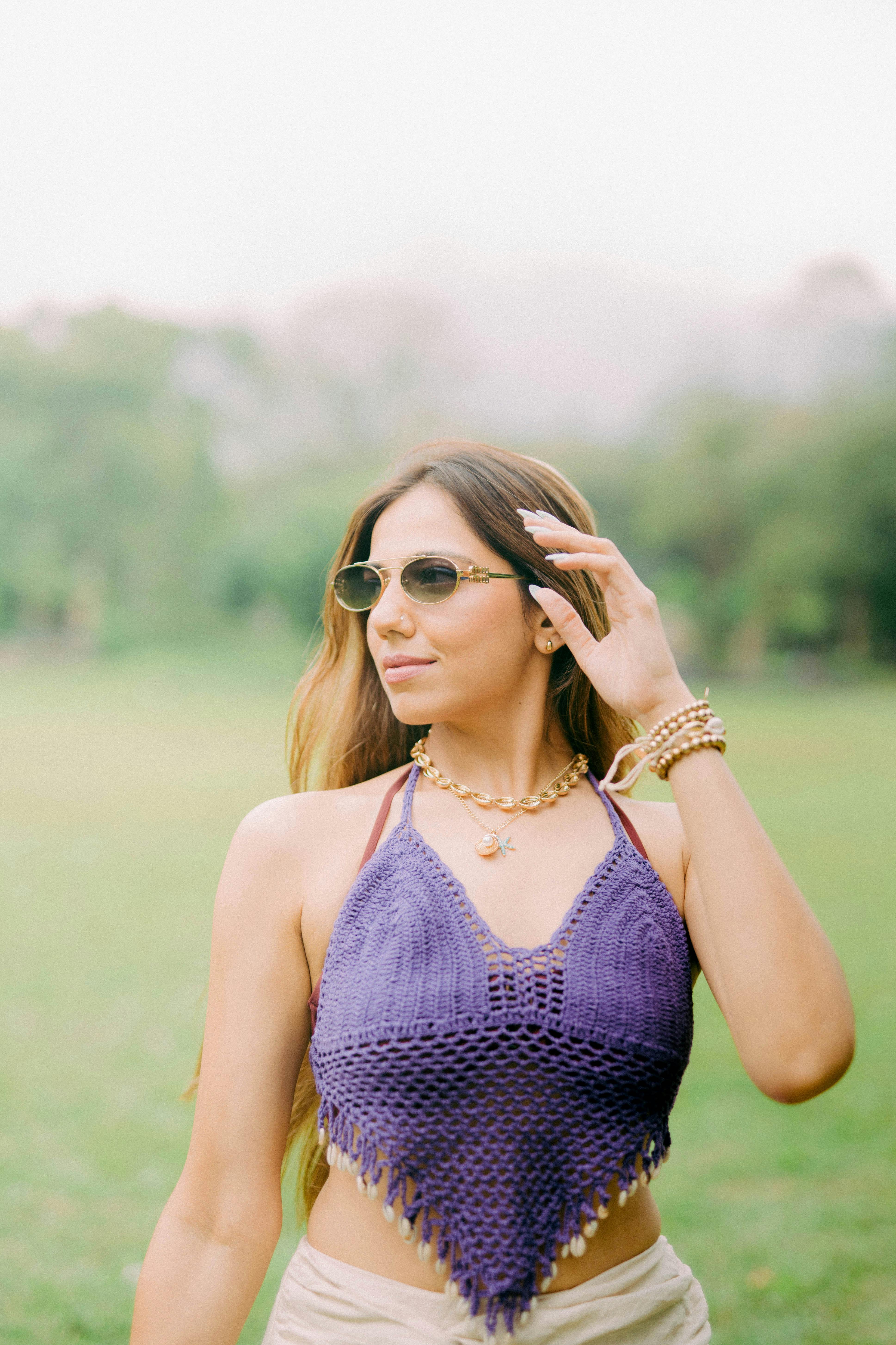 Gratis Wanita modis dengan atasan rajutan ungu dan kacamata hitam menikmati hari yang cerah di taman Bali. Foto Stok