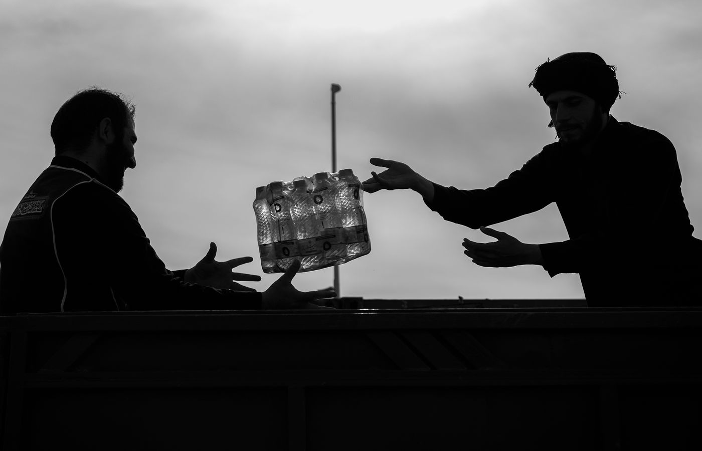 Silhouettes of two men exchanging bottled water in Mehran, Iran.