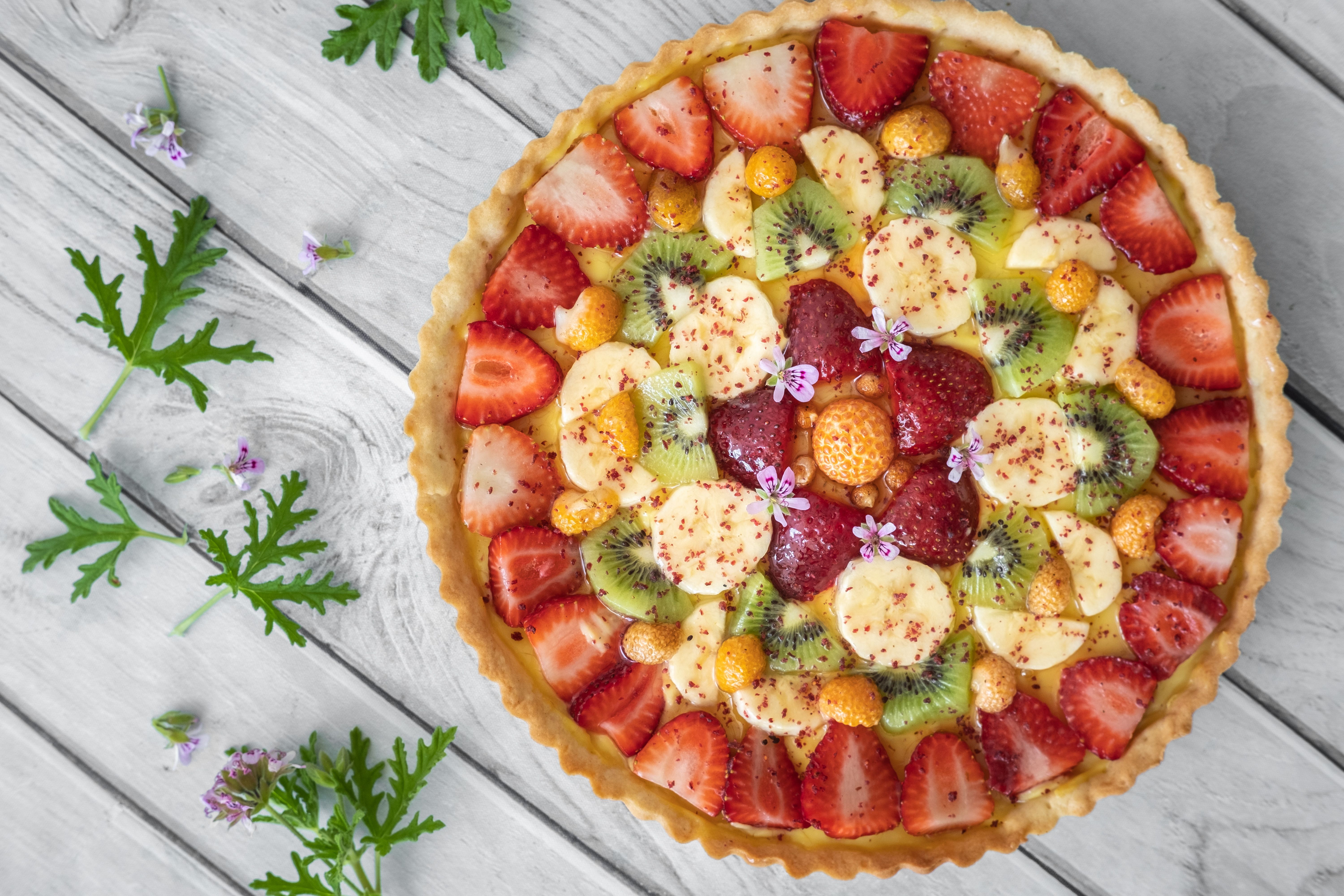 Colorful fruit tart with strawberries, kiwi, and banana on a wooden surface.
