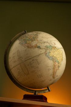A classic globe depicting North and South America, warmly lit on a wooden base. 30792656