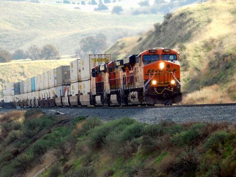 Freight train passing through scenic hills with vibrant landscape.