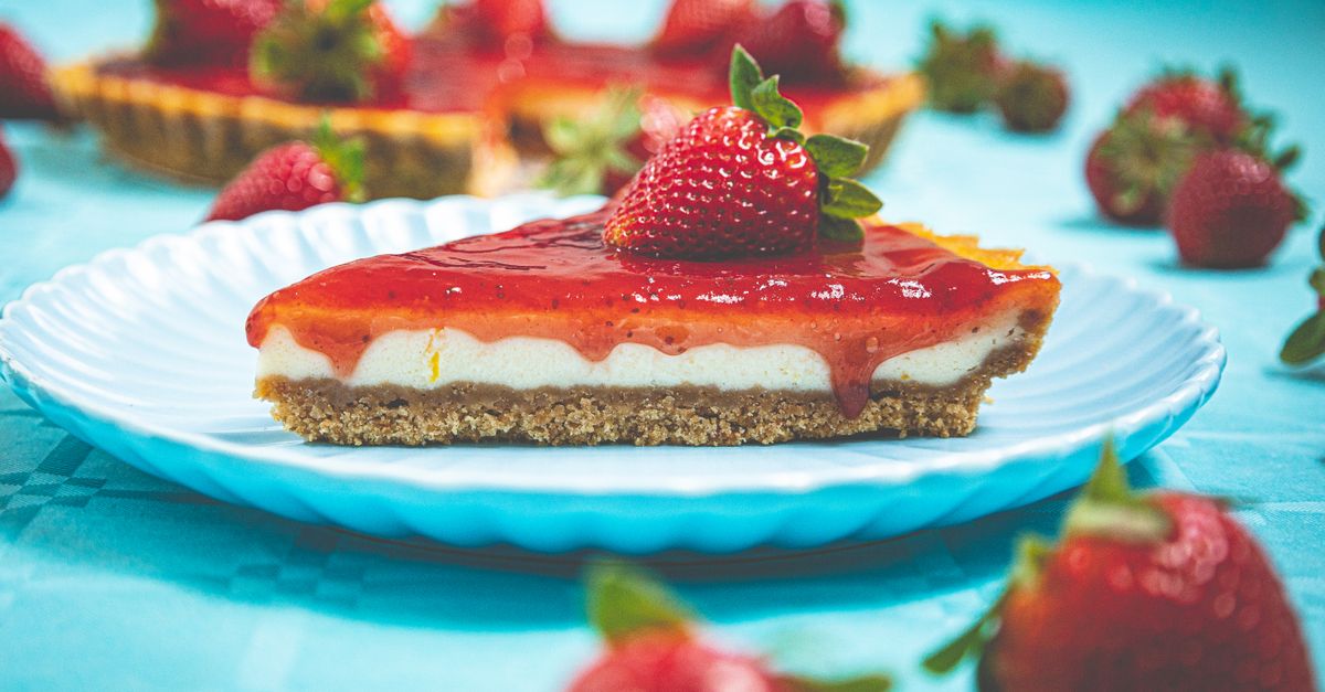 Uma tentadora fatia de cheesecake de morango decorada com morangos frescos em um prato azul.