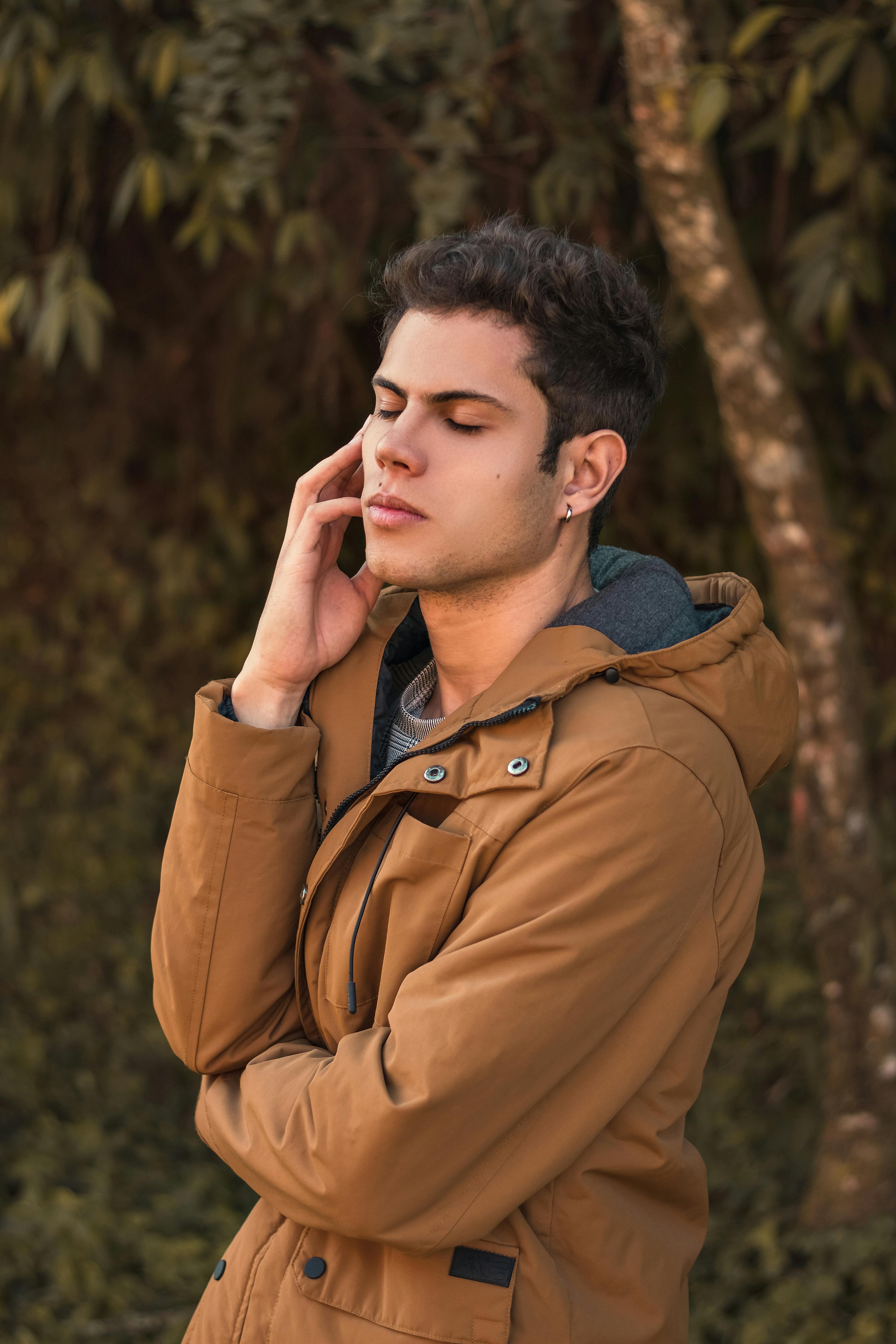 一位穿着棕色外套的时尚年轻人在自然环境中摆姿势，展现着时尚与自信