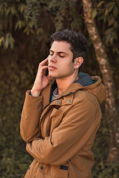 一位穿着棕色外套的时尚年轻人在自然环境中摆姿势，展现着时尚与自信