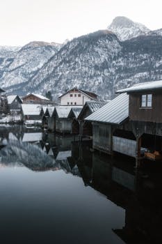 Tranquil winter scene of snow-covered village houses reflecting in a calm lake.