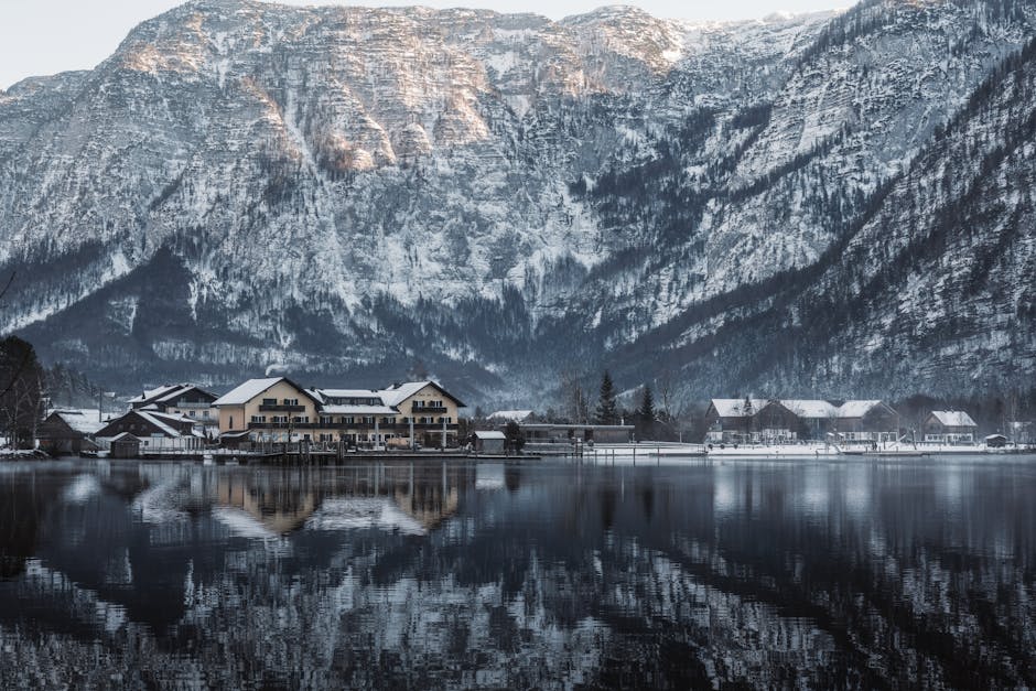 A peaceful alpine village with snow-capped mountains reflected in a tranquil lake during winter. in Hallstatt