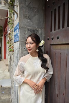 A woman in traditional attire stands gracefully by a wooden door outdoors.