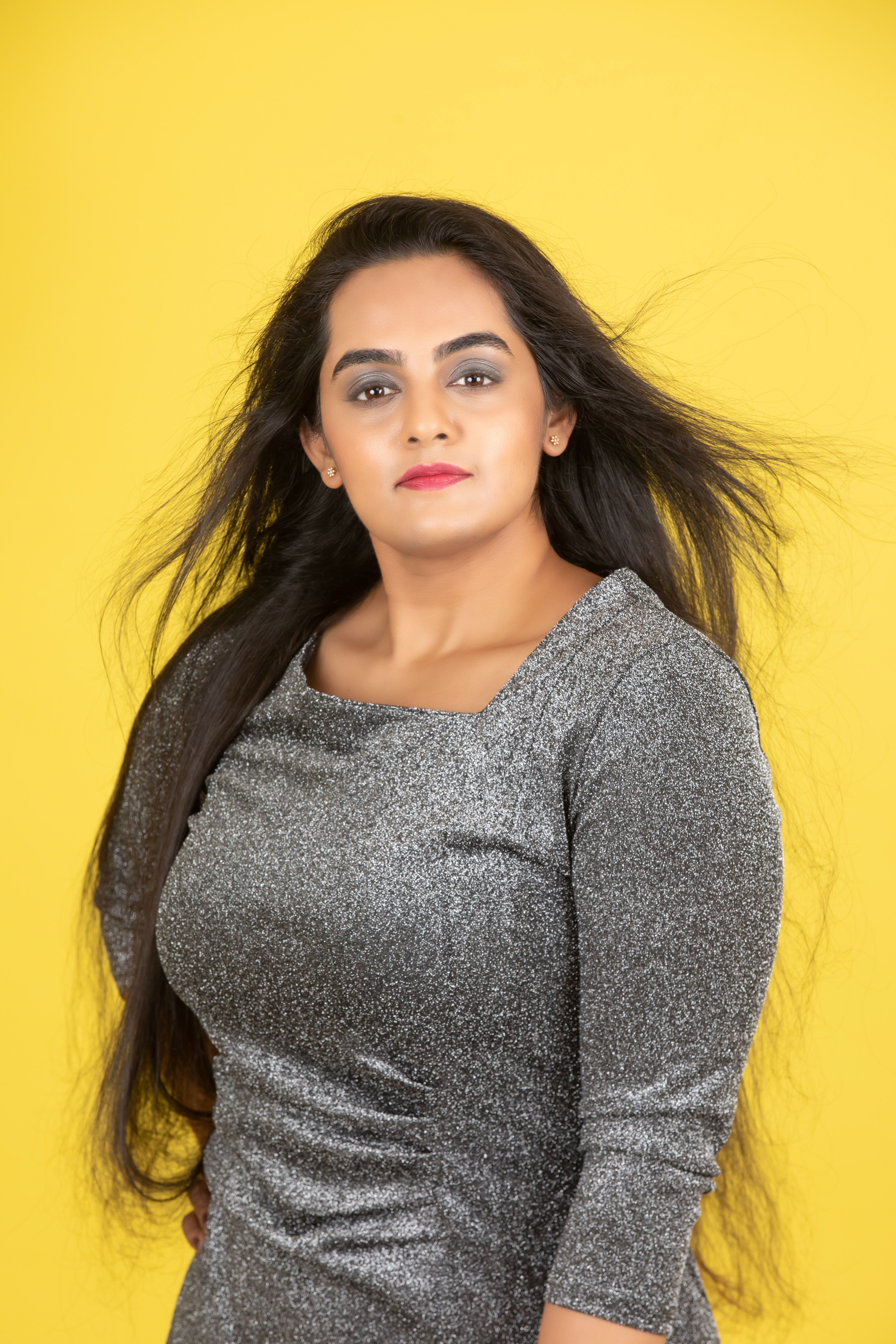 Portrait of a confident woman in a shimmering dress against a vibrant yellow backdrop.