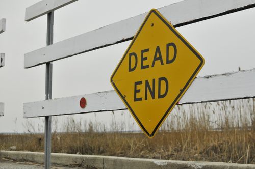 Free Yellow 'Dead End' road sign beside a white wooden fence in an outdoor rural area. Stock Photo