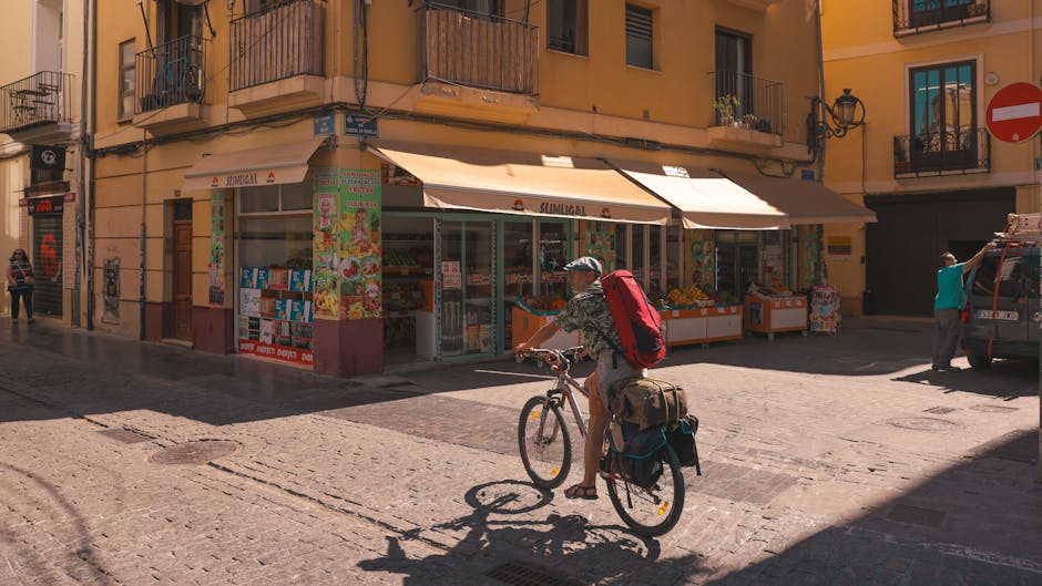 A cyclist rides past a shop in a sunny street corner in Barcelona, capturing local urban life.