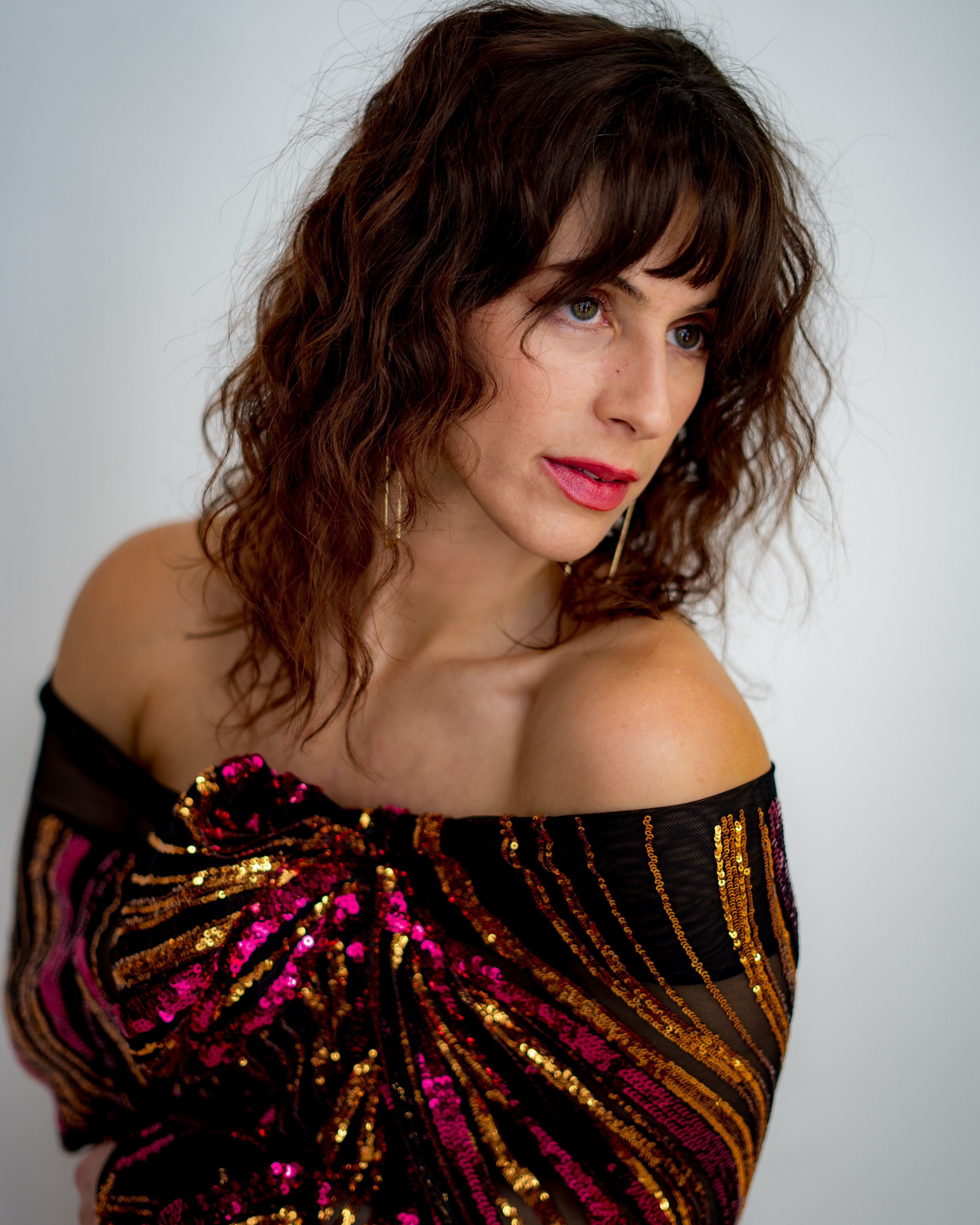 Stylish woman in vibrant sequin dress gazes thoughtfully indoors.
