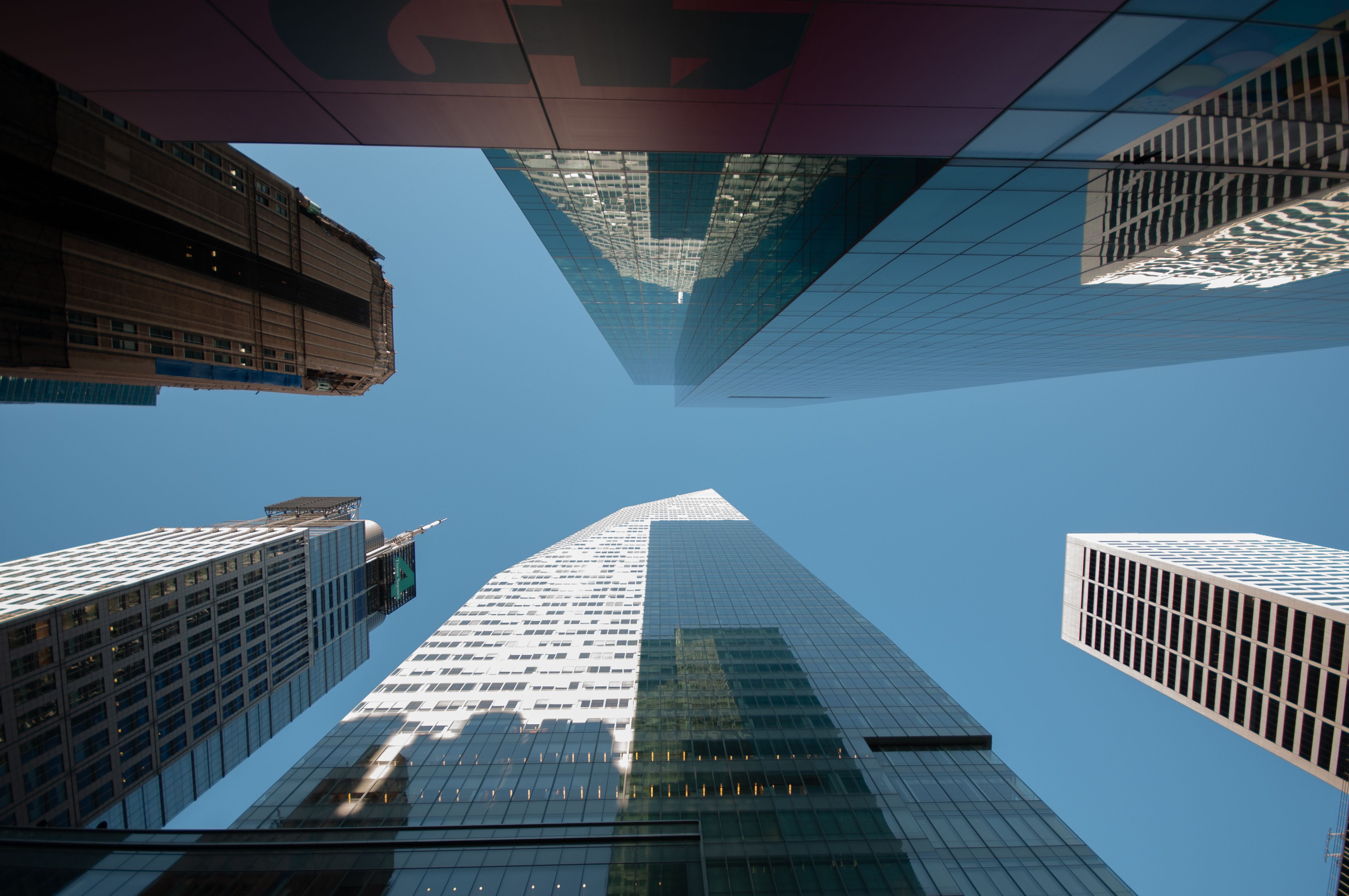 Dynamic upward view of modern skyscrapers under clear blue sky, capturing urban architecture.