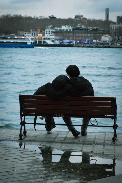 Free A couple seated on a bench by the waterfront, reflecting romantic vibes. Stock Photo