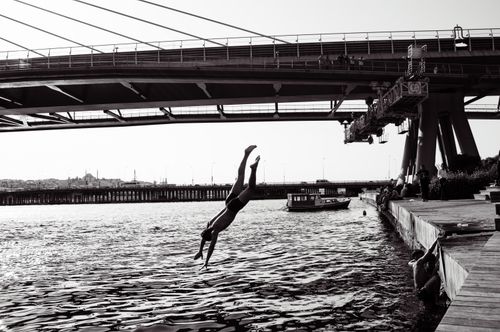 Free A silhouette of a diver leaping into the water under a bridge in İstanbul, capturing a dynamic urban scene. Stock Photo