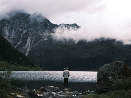 Free A lone person gazes at a serene lake surrounded by majestic mountains. Stock Photo
