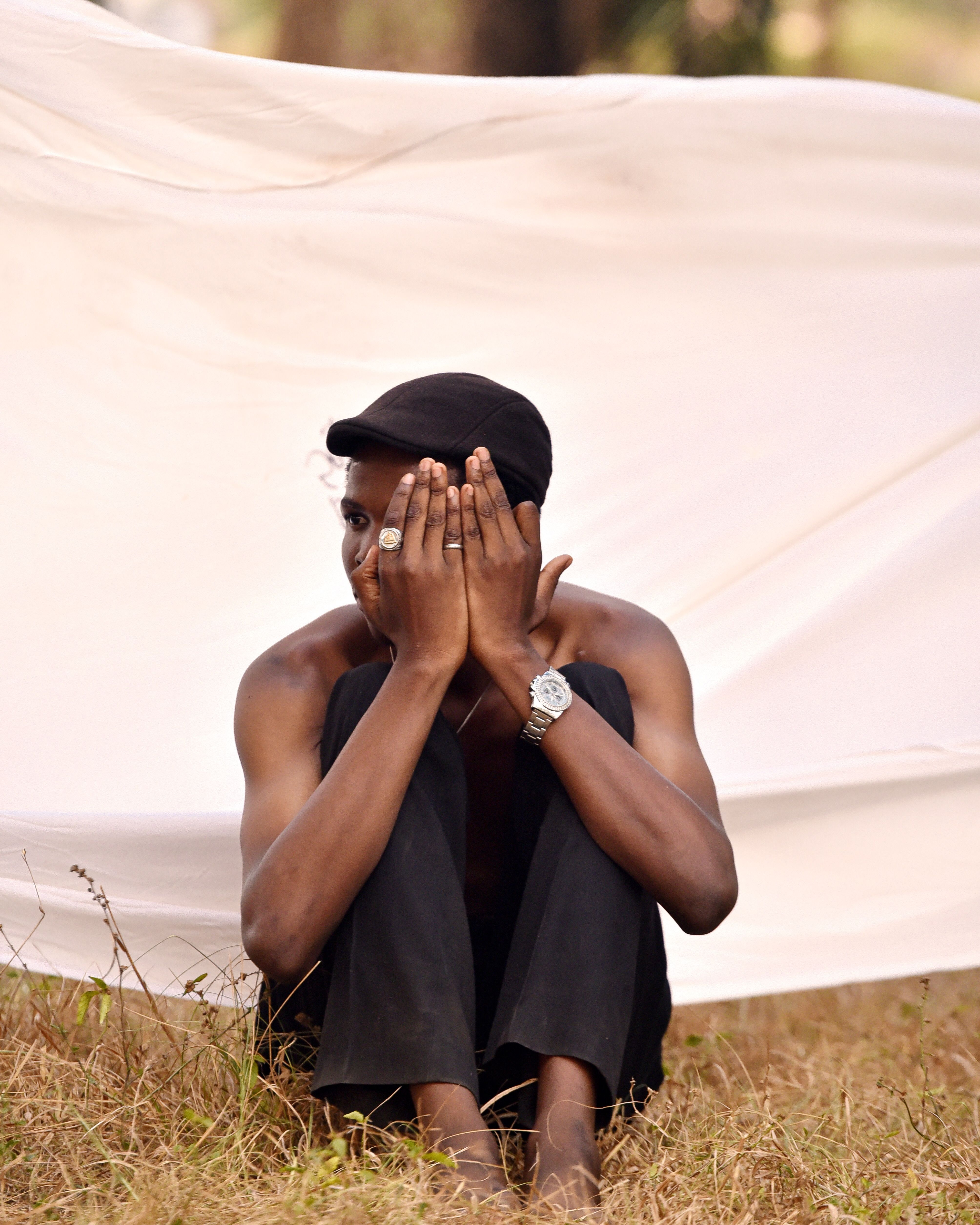 Young man sitting outdoors covering his face · Free Stock Photo