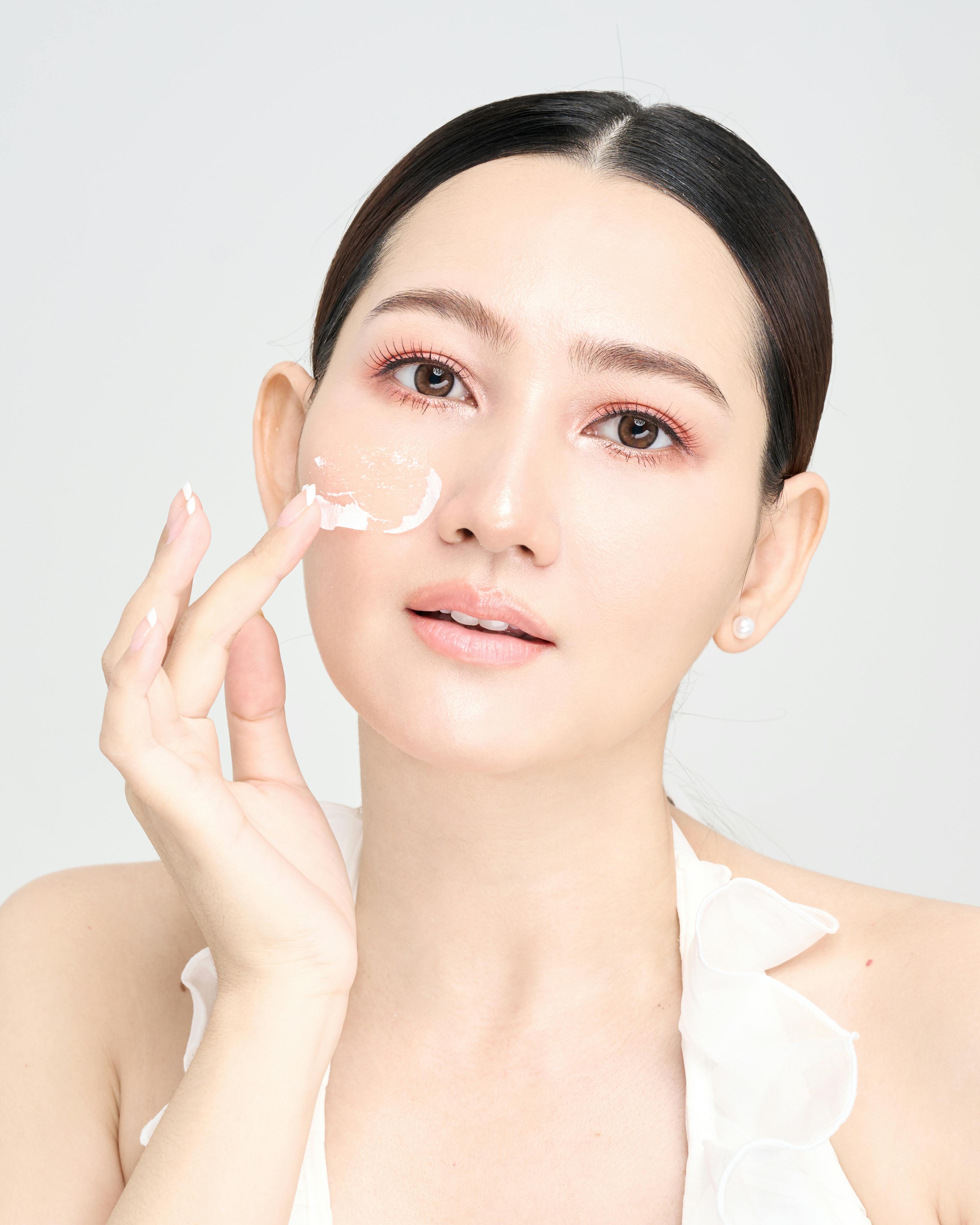A young woman applies skincare cream to her face, promoting a healthy and radiant complexion.