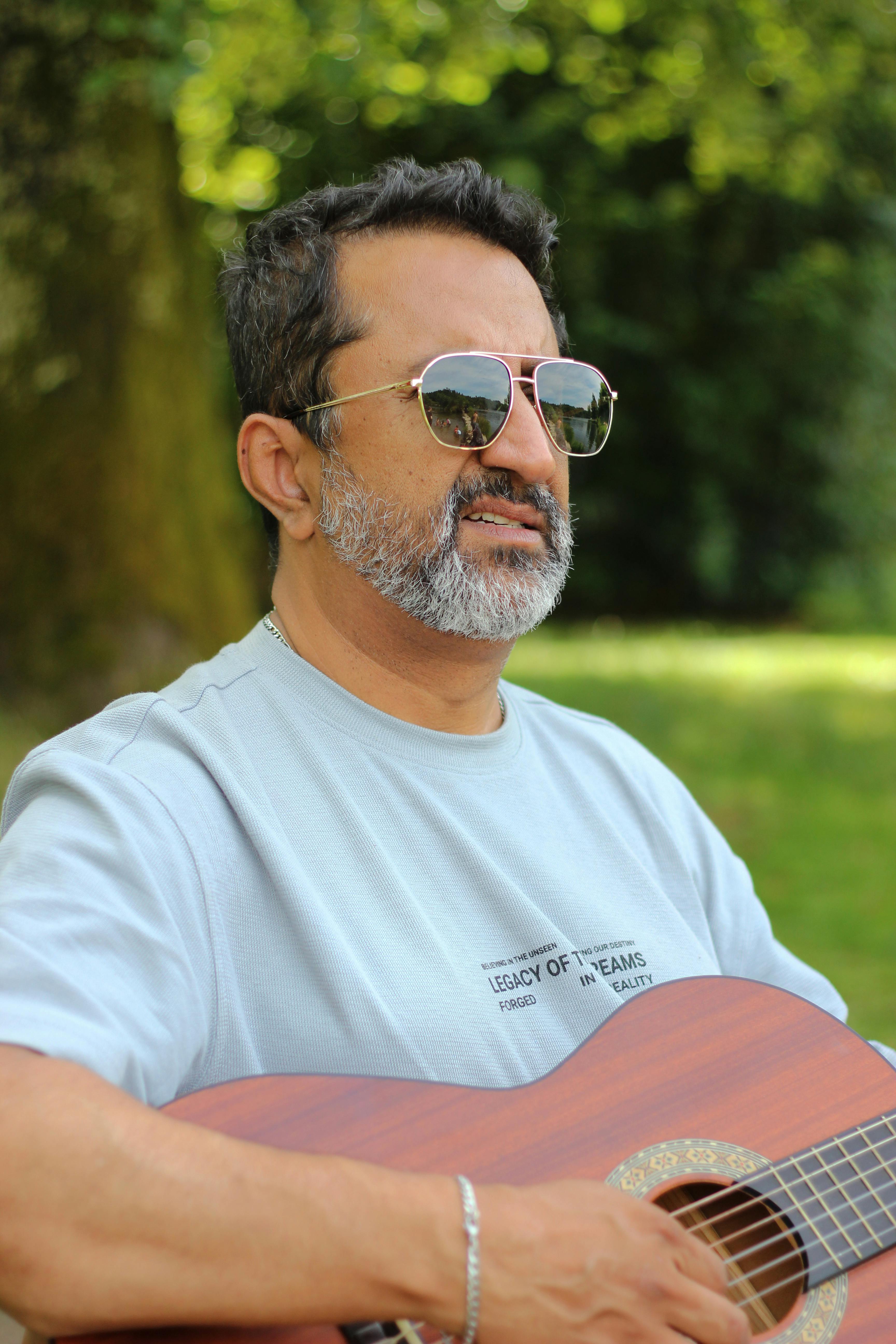 Adult male playing guitar in a sunny park setting, exuding calmness and leisure.