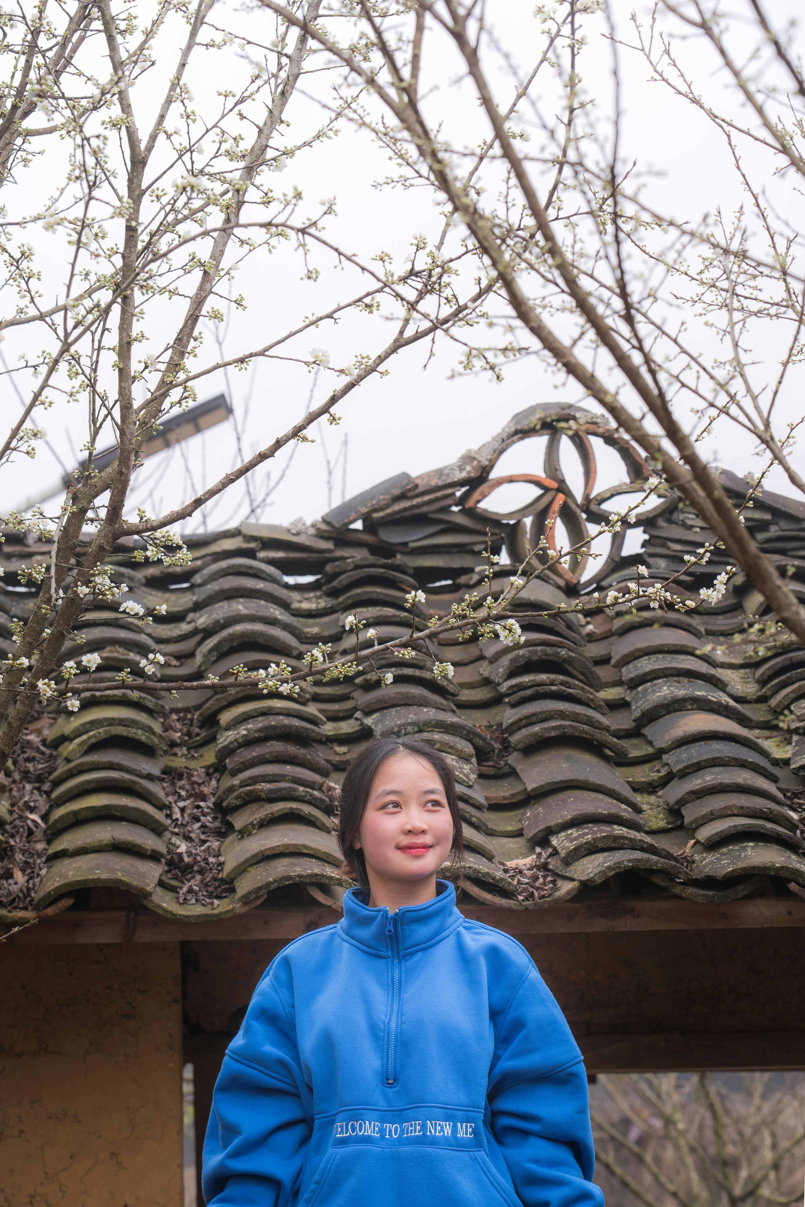 A young woman in a blue jacket stands under blooming trees, welcoming spring.