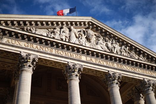 Historic Pantheon in Paris featuring detailed facade with French flag under a blue sky. Cultural landmark.