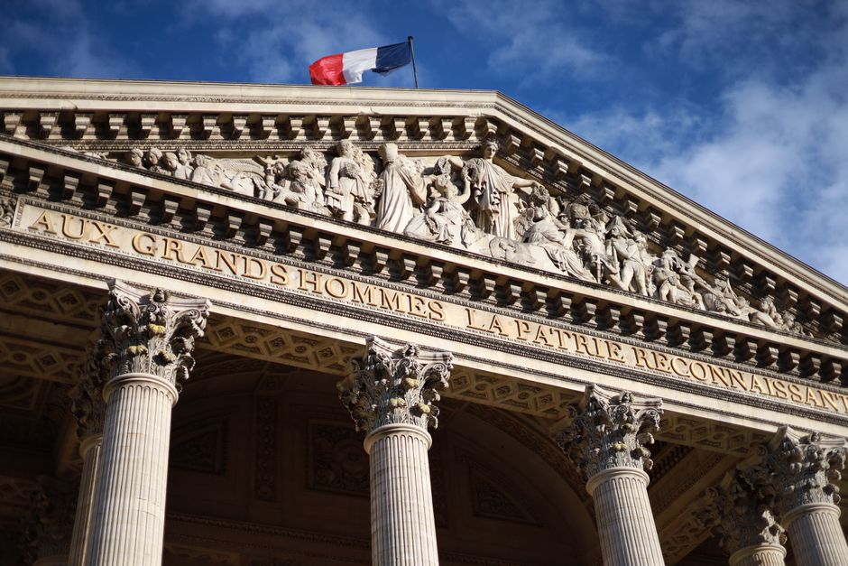 Historic Pantheon in Paris featuring detailed facade with French flag under a blue sky. Cultural landmark.