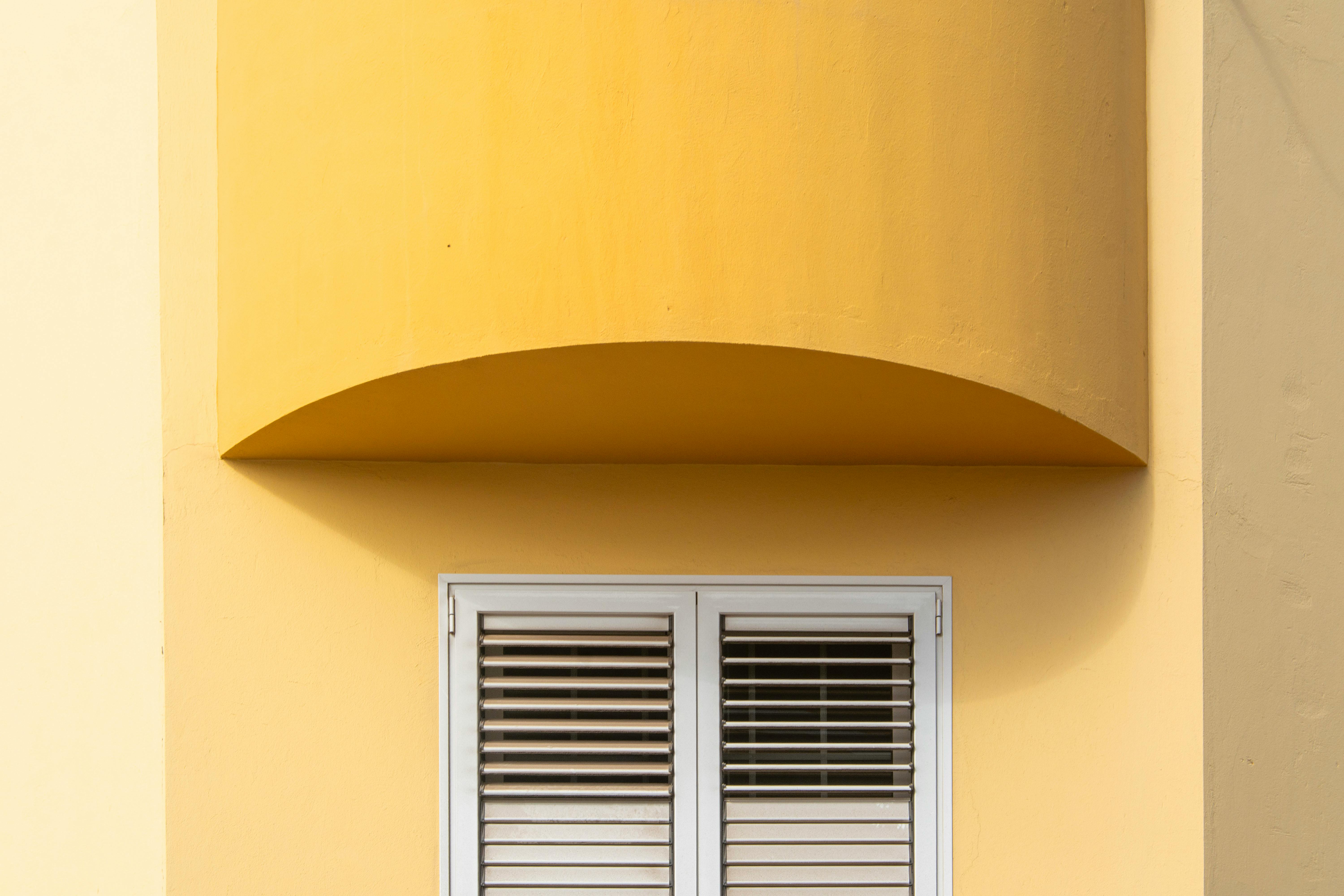 Kostenlos Nahaufnahme einer gelben Fassade mit einem modernen Fenster mit Fensterläden, das architektonisches Design zeigt. Stock-Foto