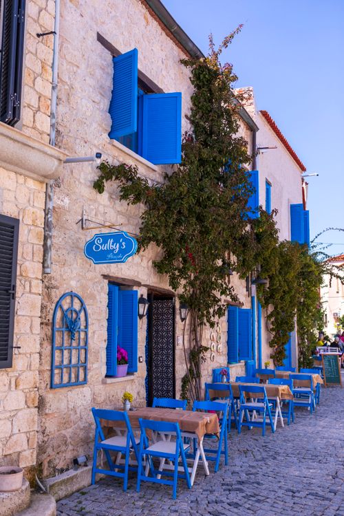 Free Cozy street café in Alacati, İzmir with rustic stone walls and vibrant blue shutters. Stock Photo