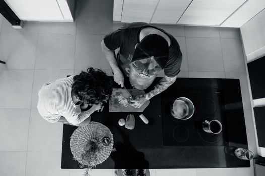 A black and white photo showing two people in a kitchen preparing a meal together.