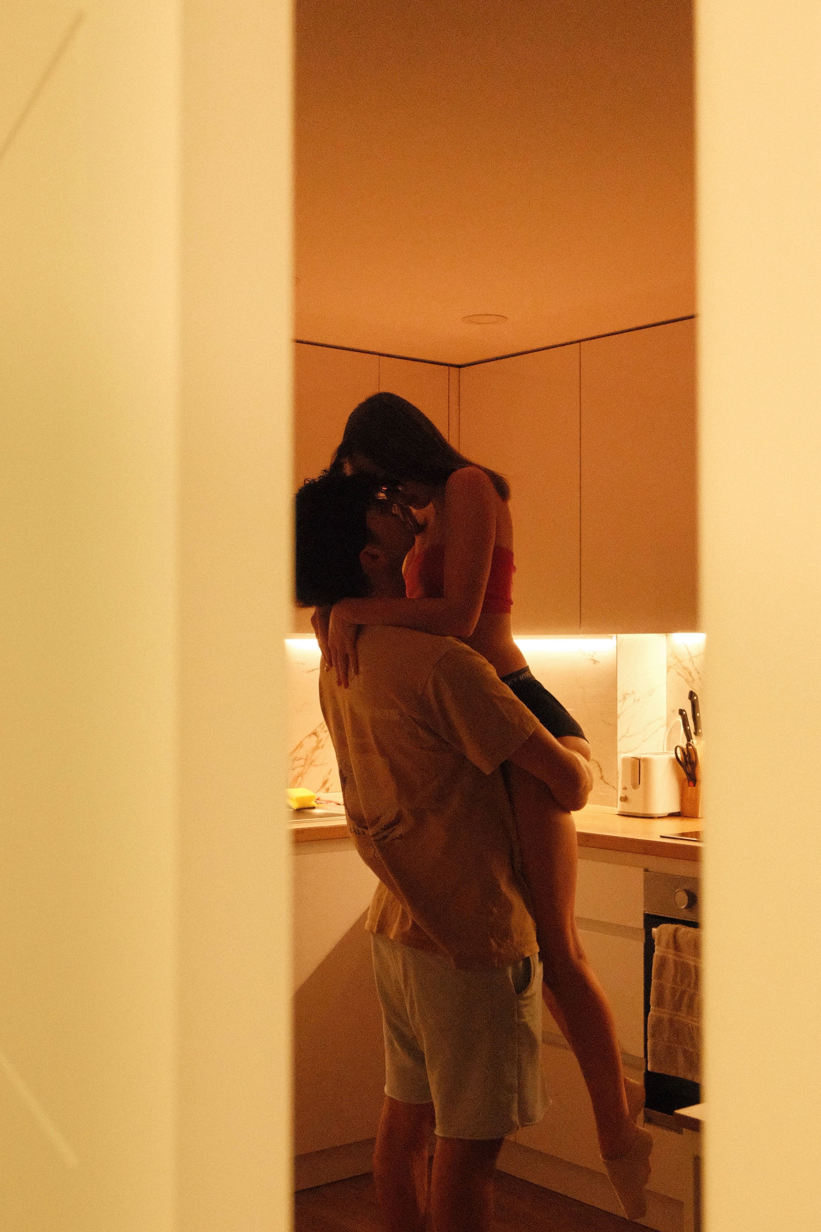 A warm intimate moment between a couple in a softly lit kitchen at night.