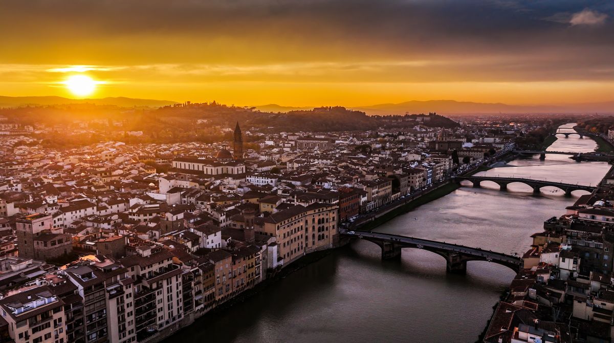 Ponte Vecchio bridge Florence at sunset with overhanging jewelry shops golden light reflecting on Arno river