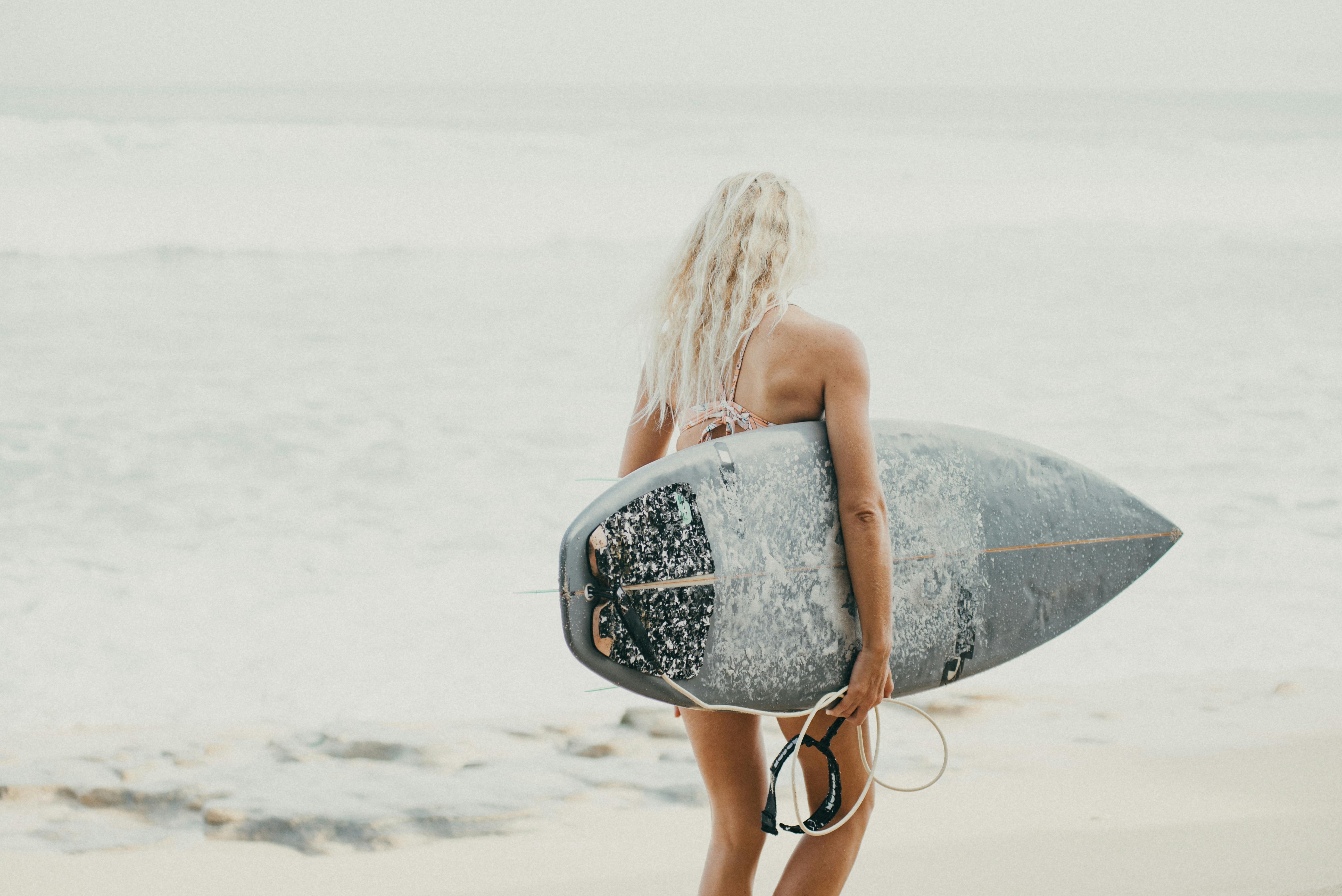 Free An adult woman carrying a surfboard walks towards the ocean on a sunny day in Bali, Indonesia. Nusa Dua Beach