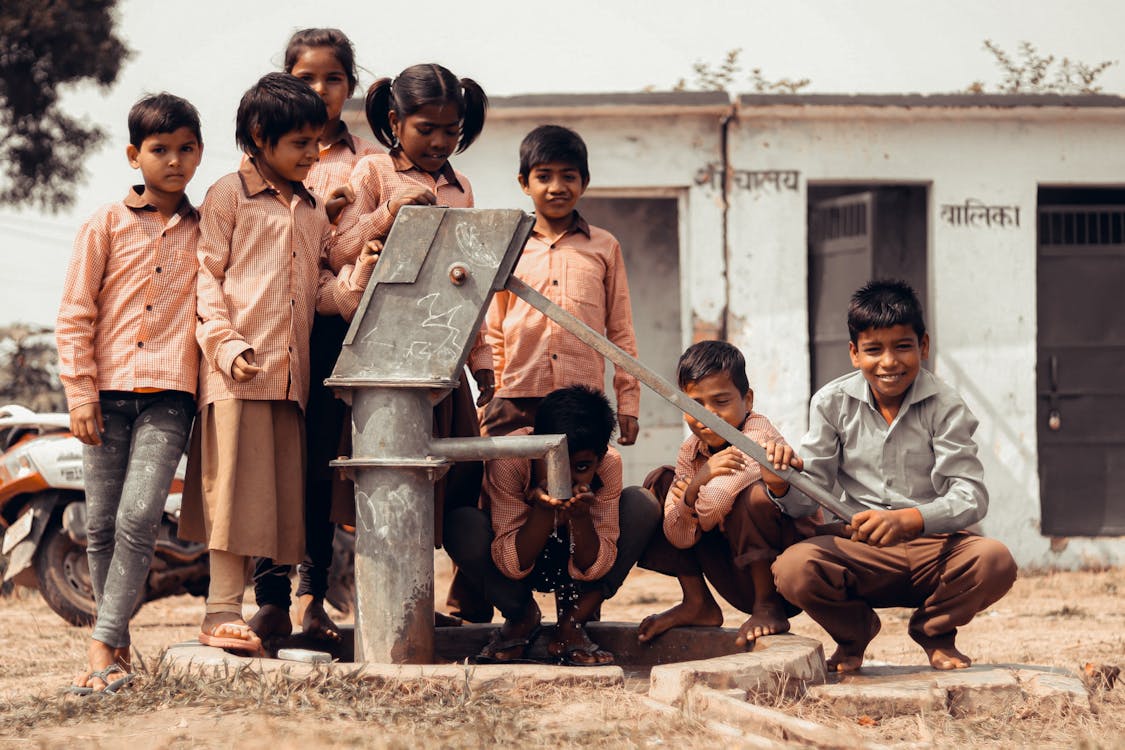 Free Children Standing next to Manual Water Pump Stock Photo