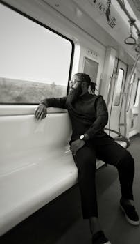Stylish man with glasses in a black outfit reflecting while traveling on a train.