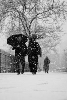 Monochrome scene of people walking in the snow, umbrellas open, in İstanbul.