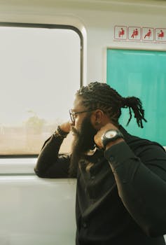 Thoughtful man with beard and dreadlocks on train, exuding modern elegance in Abuja.