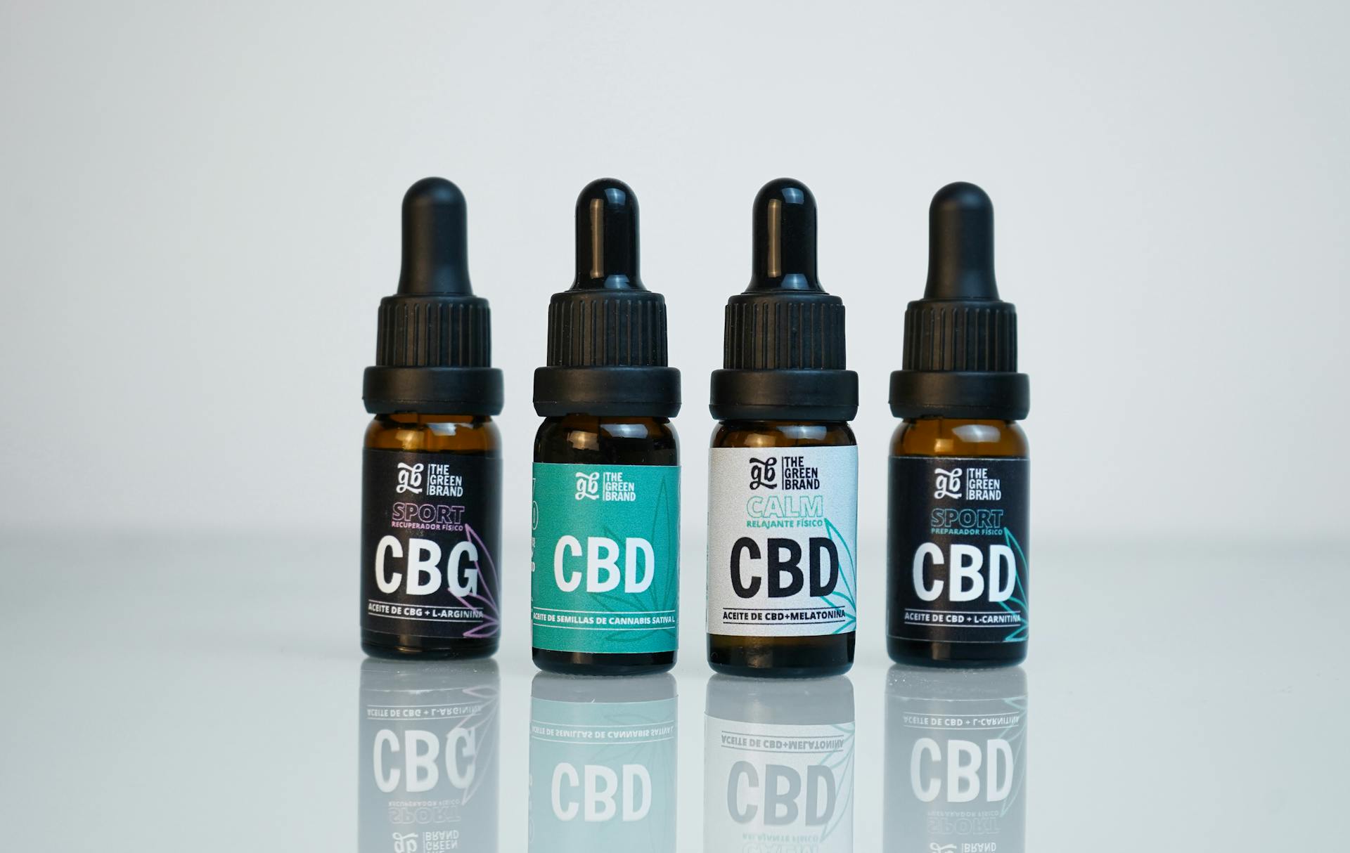 Four CBD and CBG oil bottles in a row on a reflective surface, showcasing product branding.