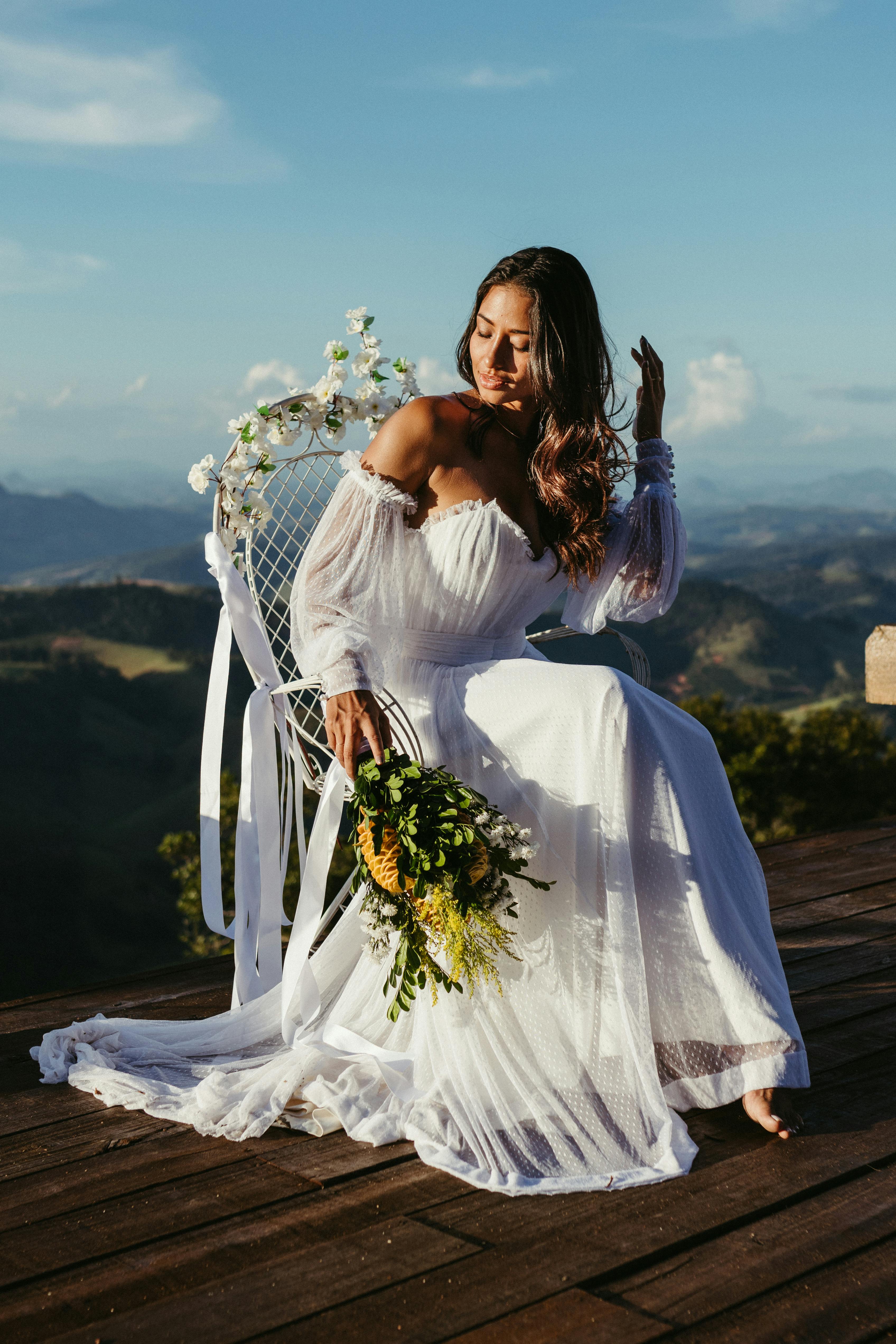 一位穿着飘逸白色连衣裙的美丽新娘在风景秀丽的山甲板上优雅地摆姿势